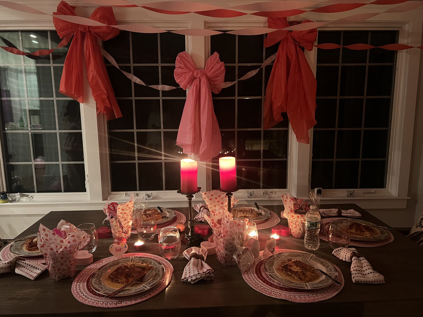 Candlelit Valentine's dinner table with pink tissue bows on the windows and heart-print napkins
