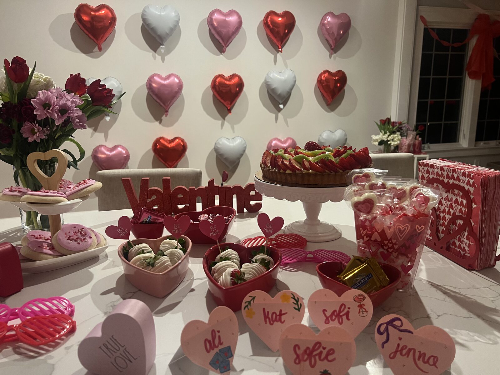 Valentine's dessert table with heart balloons, strawberry tart, chocolate-covered strawberries and Valentine sign