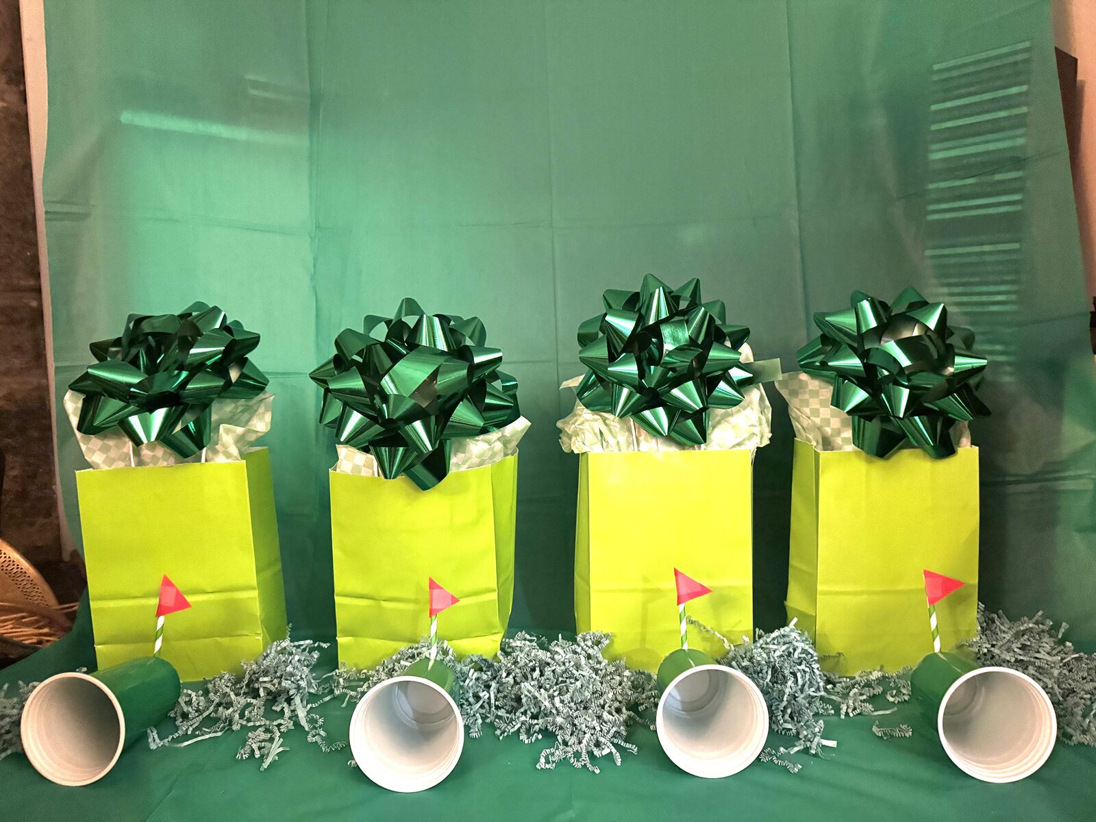Row of green golf-themed favor bags with metallic bows and tiny flag hole markers