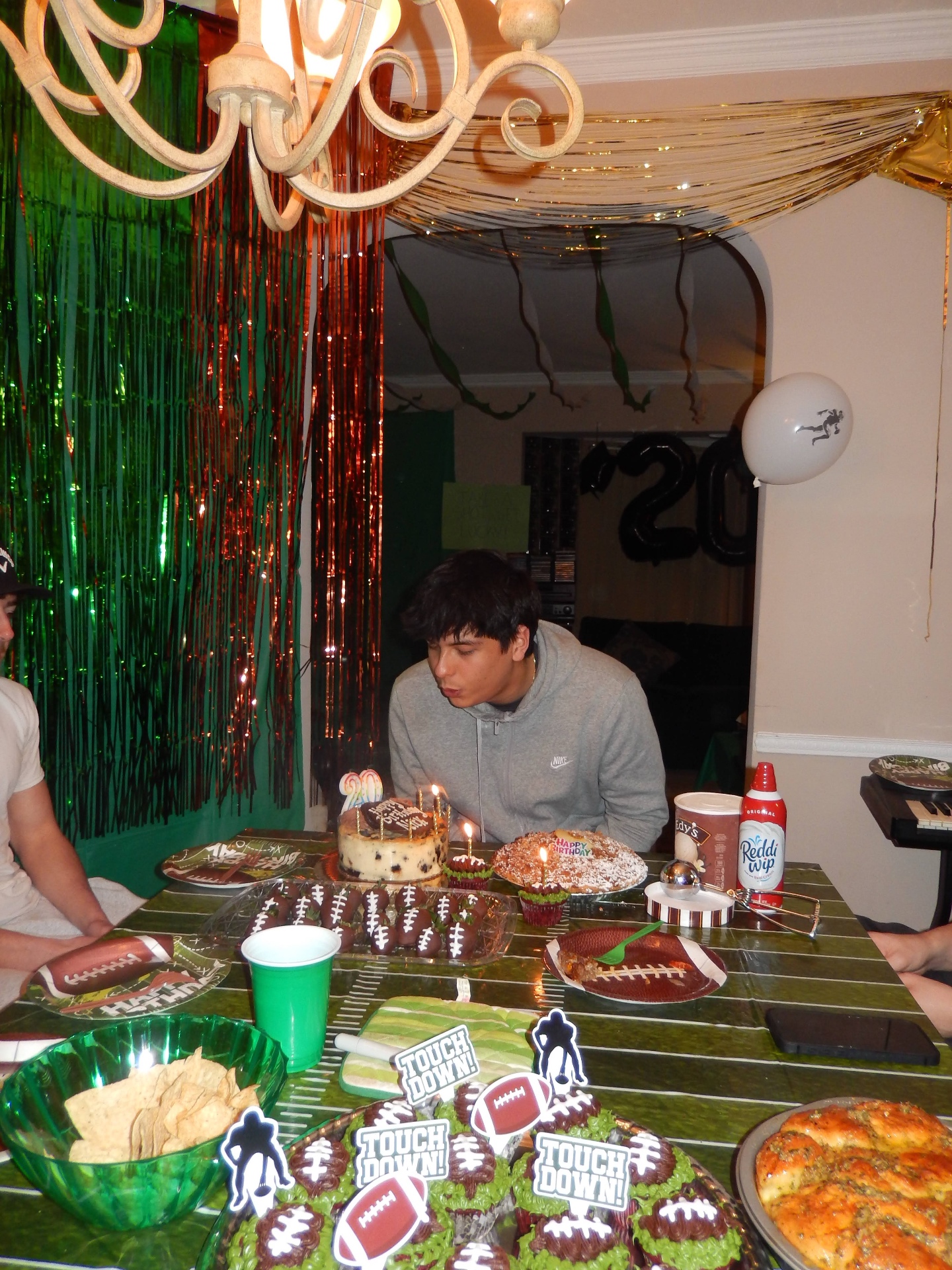 Football-themed birthday spread with green field tablecloth, foil fringe backdrop and stadium snacks