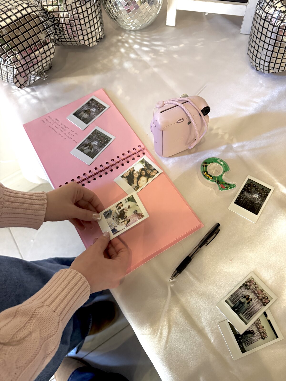 Pink instant camera with photobook and instant photos arranged on a satin tablecloth
